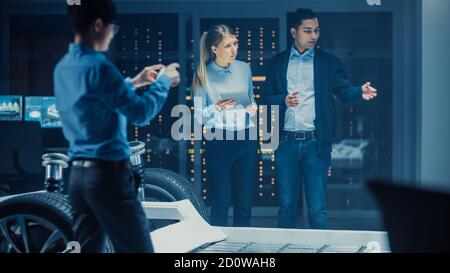 Foto di una sala laboratorio di sviluppo con un team professionale diversificato Di ingegneri e scienziati che lavorano su un telaio per auto elettriche Con ruote Foto Stock