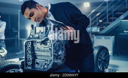 Sala laboratorio di sviluppo con un tecnico di progettazione automobilistica professionista che lavora su una trasmissione di ingranaggi di automobile elettrica. Telaio con ruote, batterie Foto Stock