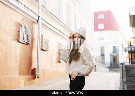 Affascinante giovane donna dai capelli marroni su una passeggiata. Una donna bella e felice in un'immagine elegante in un cappello a maglia calda. Passeggiate per la città, stile di vita Foto Stock