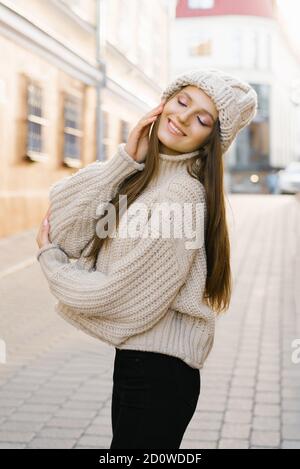 Affascinante giovane donna dai capelli marroni su una passeggiata. Una donna bella e felice in un'immagine elegante in un cappello a maglia calda. Passeggiate per la città, stile di vita Foto Stock