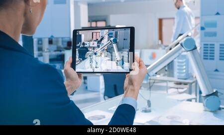 L'elegante ingegnere di robotica industriale femminile utilizza un Tablet computer per registrare un video del braccio robot mobile utilizzato per sollevare e spostare oggetti. Tecnologia Foto Stock