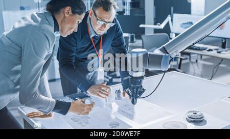 Elegante Ingegnere femminile e Specialista maschile parla Lean sul tavolo lavoro con Blueprint, documenti e Tablet computer. Operazioni sul programma e. Foto Stock