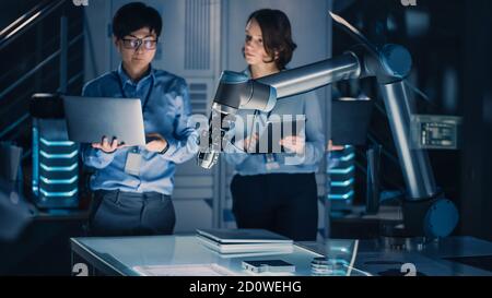 Uomo e donna ingegneri con notebook e tablet analizzare e discutere come un braccio robotico futuristico funziona e muove un oggetto metallico. Sono in alto Foto Stock