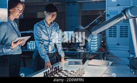 Due ingegneri di sviluppo stanno discutendo e testando un'interfaccia di intelligenza artificiale giocando a Scacchi con un braccio robotico futuristico. Sono dentro Foto Stock