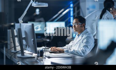 Maschile IT Scientist utilizza un computer che mostra il programma di monitoraggio e controllo del sistema. In background Technology Development Laboratory con gli scienziati Foto Stock