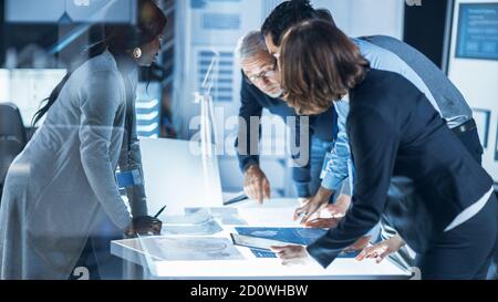 Incontri di ingegneri nel laboratorio di Ricerca tecnologica: Ingegneri, scienziati e sviluppatori si sono riuniti intorno illuminato tavolo da conferenza, parlare e. Foto Stock