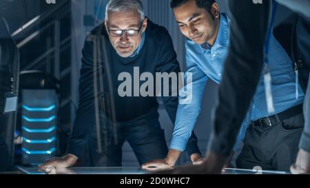 Incontri di ingegneri nel laboratorio di Ricerca tecnologica: Ingegneri, scienziati e sviluppatori si sono riuniti intorno illuminato tavolo da conferenza, parlare e. Foto Stock