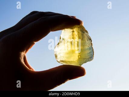 Persona mano che tiene una pietra di cristallo di quarzo giallo limone verde contro il sole e il cielo blu. Lucido, spazio per la copia. Foto Stock