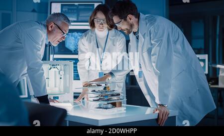 Shot in Industrial Design Laboratory, Specialist utilizza Microscope, Designer Works su Personal computer, ricercatore scrive su Glass Whiteboard, Team di Foto Stock