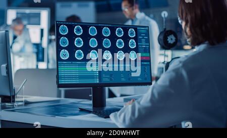 Foto a spalla: La scienziata IT femminile utilizza un computer che mostra il programma di monitoraggio e controllo del sistema. In background sviluppo tecnologico Foto Stock