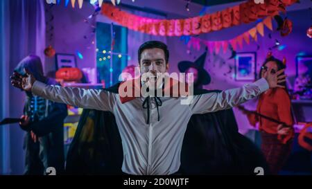 Halloween Costume Party: Conte Dracula indossare il suo capo fa Vampire Dance, in background bella strega, splendida lei diavolo e paura Foto Stock