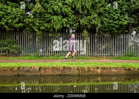Un jogger grigio dai capelli corre lungo l'alzaia del Bridgewater Canal in sale Foto Stock