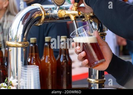 Primo piano di un barista che versa birra alla spina fresca in una tazza di plastica durante un festival all'aperto. Una lager fresca e schiumosa viene servita da una spina Foto Stock