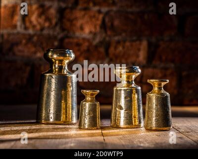 Set di pesi in ottone e piombo vintage 1800 da 4 pz e gli agenti atmosferici su pavimento di legno con sfondo di mattone Foto Stock