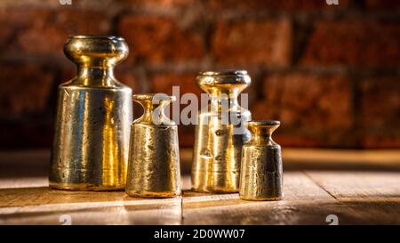 Set di pesi in ottone e piombo vintage 1800 da 4 pz e gli agenti atmosferici su pavimento di legno con sfondo di mattone Foto Stock