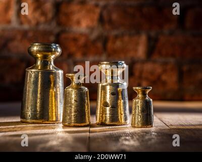 Set di pesi in ottone e piombo vintage 1800 da 4 pz e gli agenti atmosferici su pavimento di legno con sfondo di mattone Foto Stock