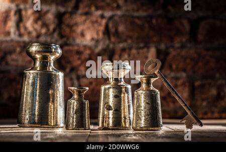 Set di pesi in ottone e piombo d'epoca del 1800 di 4 pz, con fodero e intemperie con chiave arrugginita su pavimenti in legno con fondo in mattoni Foto Stock