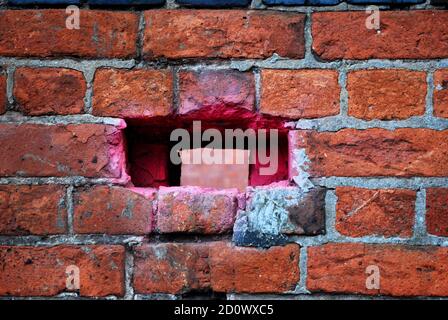 Un buco in un muro di mattoni che è stato spray verniciato rosa Foto Stock