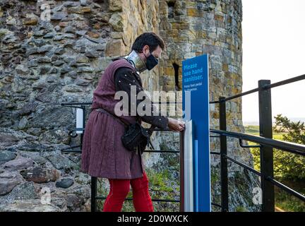 Uomo che indossa una maschera in costume medievale con igienizzatore a mano, il castello di Dirleton, East Lothian, Scozia, Regno Unito Foto Stock