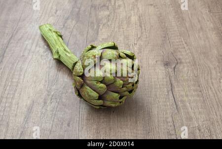 Un carciofo viola organico fresco con dettagli a stelo su a. rustica superficie in legno e. Foto Stock