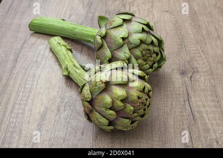 Due carciofi viola organici freschi con dettagli a stelo su A. rustica superficie in legno Foto Stock