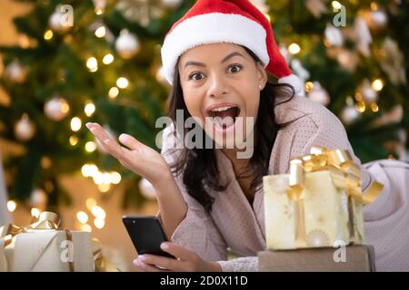 Scioccata donna biraciale stupito dal messaggio di vendita di Natale su cella Foto Stock