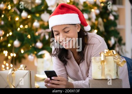 Donna biraciale felice in cappello di santa utilizzando smartphone gadget Foto Stock