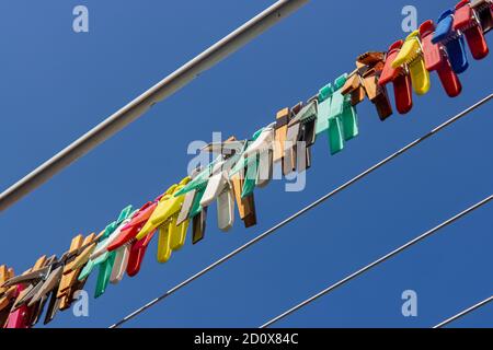 Un pig colorato di vestiti appeso su un filo di cremagliera di asciugatura. Un gruppo di stendibiancheria in linea contro il cielo blu. Foto Stock