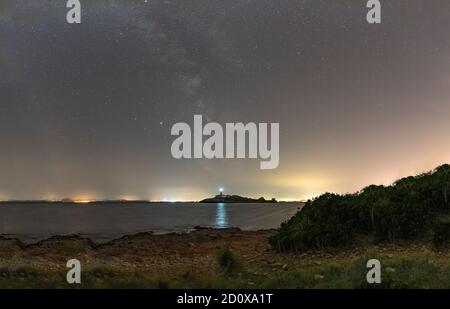 Via Lattea sul faro Aucanada, nella baia di Alcudia, Maiorca, Spagna, in una notte estiva e cielo limpido. Immagine tratta dalla spiaggia. Foto Stock