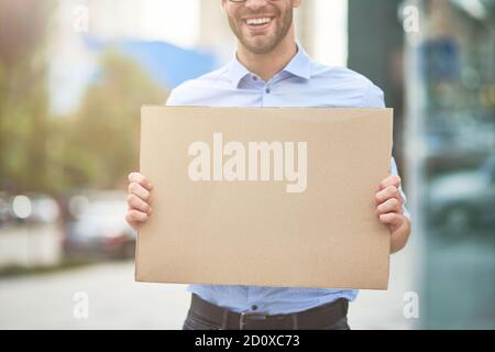 Primo piano di un attivista maschile sorridente che indossa il blu camicia e occhiali che tengono una tavola vuota mentre protestano all'aperto Foto Stock