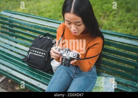 Ritratto di giovane donna asiatica utilizzando una telecamera digitale professionale nel parco all'aperto. Concetto di fotografia. Foto Stock