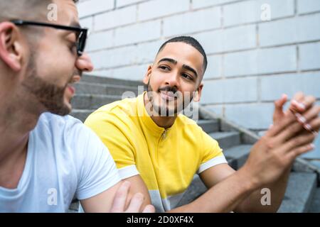 Ritratto di felice coppia gay di trascorrere del tempo insieme seduti sulle scale all'esterno. Lgbt e il concetto di amore. Foto Stock