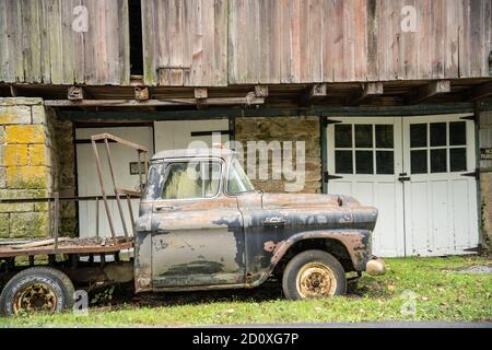 Berks County, Pennsylvania, 21 settembre 2020: Vecchio camion GMC arrugginito parcheggiato sotto il granaio rosso rustico Foto Stock