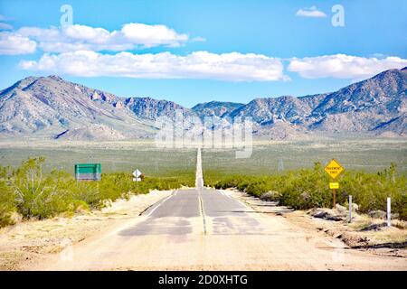 Lunga strada vuota diritta e aperta al centro della deserto che conduce alle montagne Foto Stock