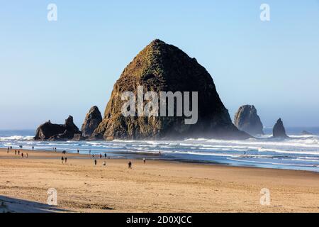 Bassa marea sulla costa dell'Oregon con persone che camminano vicino a Haystack Rock. Foto Stock