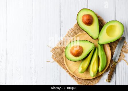 Vista dall'alto di Avocado su piastra di legno e sfondo di legno bianco con spazio per la copia. Avocado fresco maturo Foto Stock
