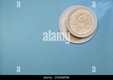 Alcuni degli ingredienti per l'impasto cucinati in piatti bianchi. Farina sale di lievito e lievito in polvere. Su sfondo blu. Foto Stock