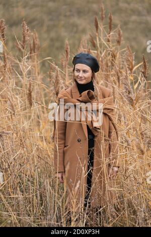 Ritratto di un bel modello giovane in un beretto nero lucido e un cappotto di lana beige Godetevi il giorno, su campo di sfondo nel soleggiato giorno d'autunno. Il concetto di Foto Stock