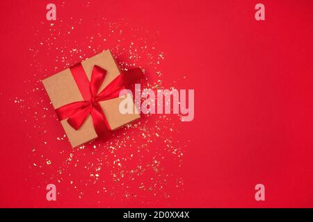 Confezione regalo con arco rosso su sfondo rosso luminoso con scintille dorate intorno e copyspace per il tuo testo. Sfondo festivo per il tuo progetto. Disposizione piatta Foto Stock