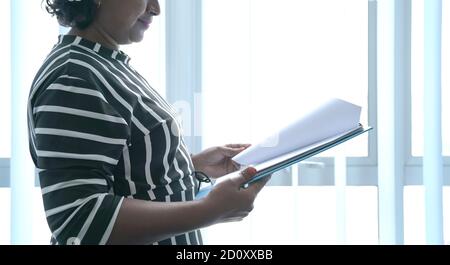 Donna d'affari che tiene e gira le pagine di un file in mano. Sfondo tendine parasole. Foto Stock