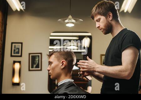 Acconciatore che fa un taglio di capelli per un giovane uomo dentro un barbiere Foto Stock