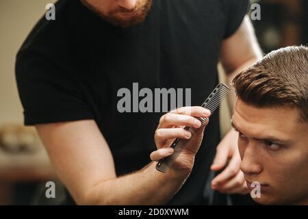 Primo piano immagine parrucchiere pettinatura dei capelli di un giovane uomo in un barbiere Foto Stock