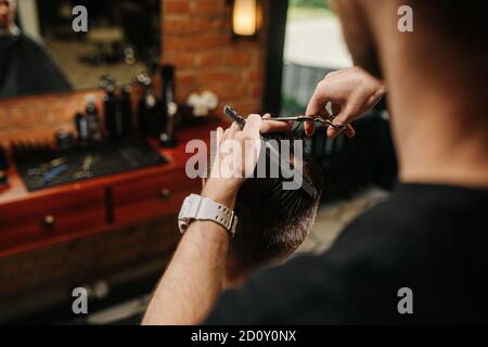 Parrucchiere artigianale che fa un taglio di capelli per un giovane uomo dentro un barbiere Foto Stock