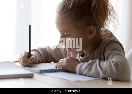 Primo piano su serio bambina scrivere in notebook, studio Foto Stock