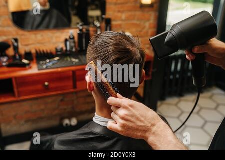 Le mani dell'uomo asciugano i capelli del giovane uomo in un barbiere Foto Stock