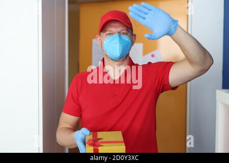 Il corriere maschio in uniforme rossa tiene il regalo nelle sue mani Foto Stock