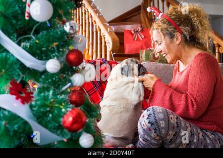 Divertente Natale tempo con coppia alternativa donna adulta e. divertente cane pug insieme divertendosi sul divano vicino l'albero di natale - inverno ho Foto Stock
