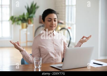 Calma giovane donna indiana meditare sul posto di lavoro Foto Stock