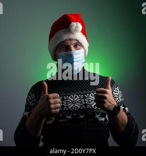 Un uomo in un cappello di Santa e una maschera medica dà un pollice in su, Foto Stock