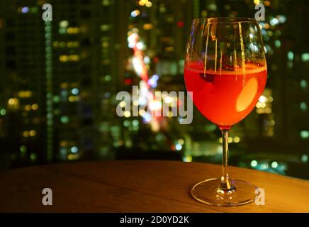 Bicchiere di cocktail rosso vivo isolato sulla terrazza panoramica tavolo con vista notturna urbana sfocata sullo sfondo Foto Stock